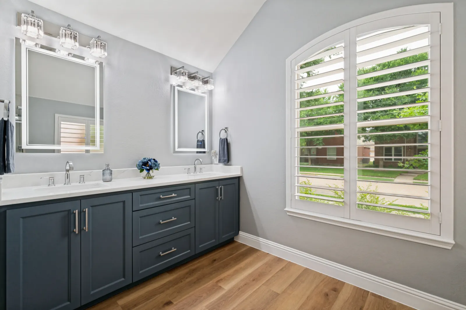 Navy double vanity with crystal sconces and arched plantation shutters