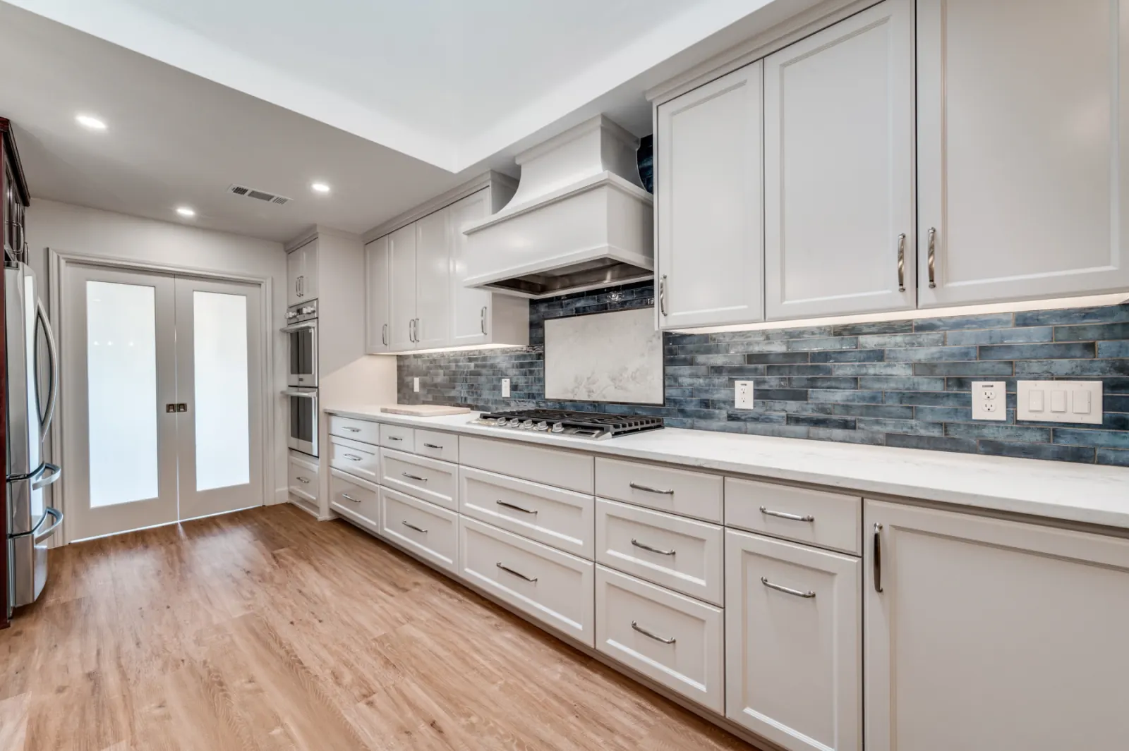 Galley kitchen with blue tile backsplash and warm wood floors
